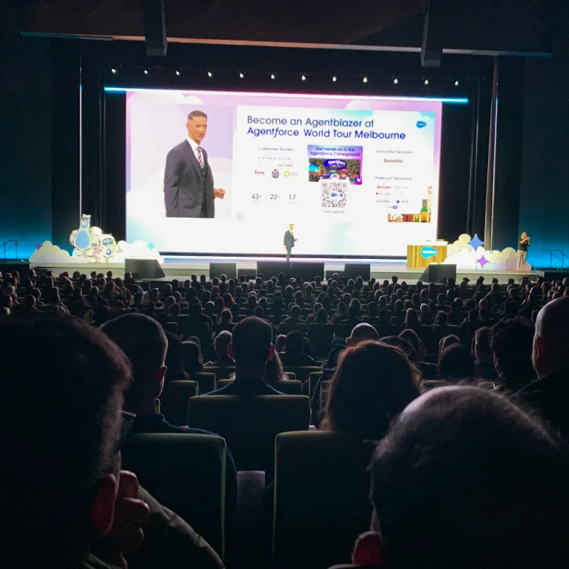 View from the audience onto the stage with the host and a screen showing a presentation about Agentblazer