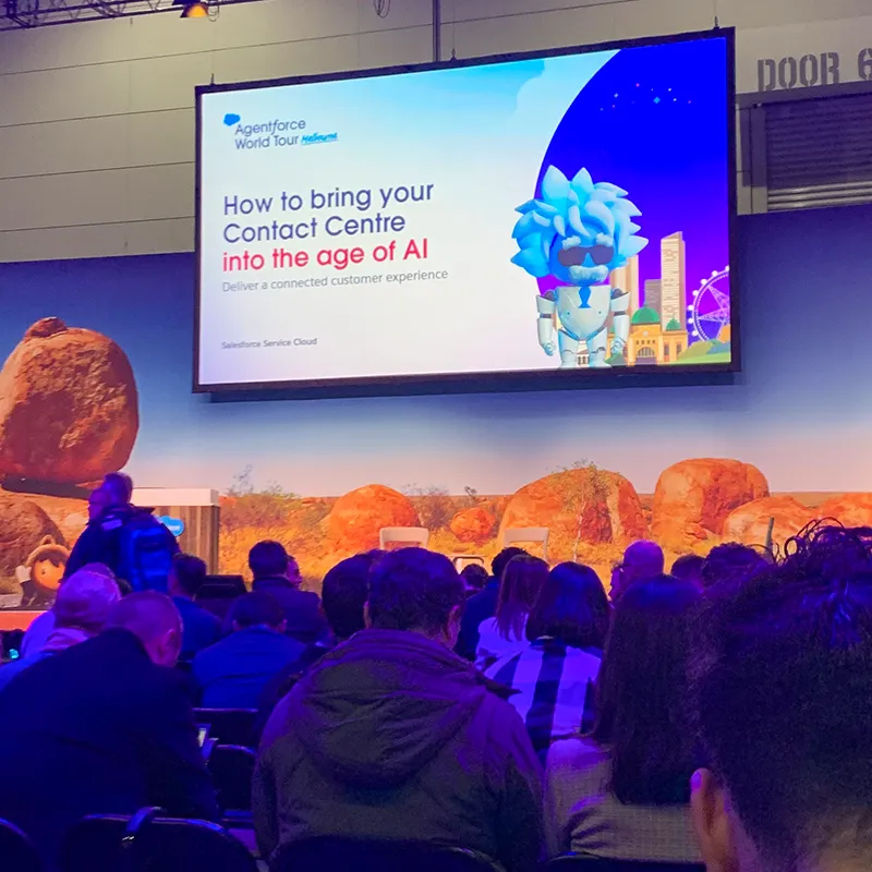 View from the audience onto a screen displaying a slide titled "How to bring your Contact Centre into the age of AI"